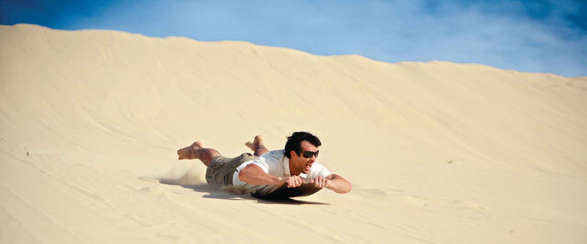 Man sandboarding down sand dune